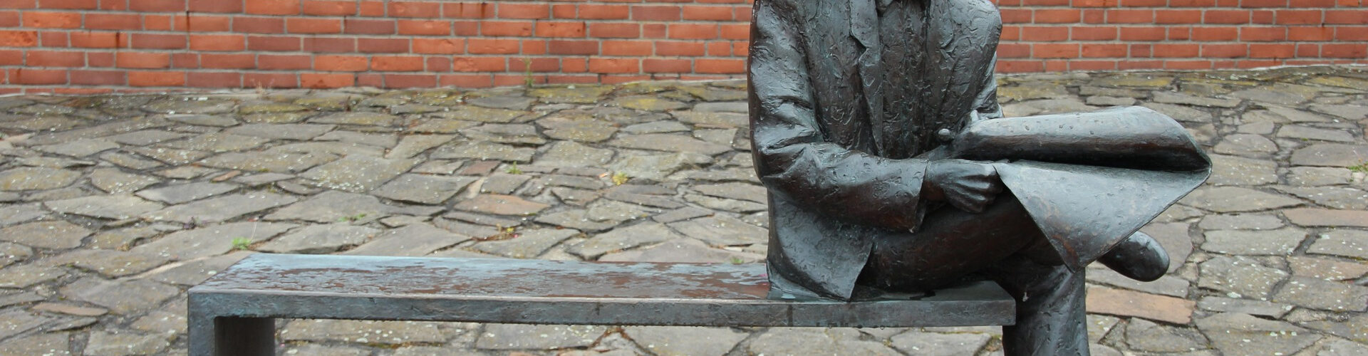 Statue représentant un homme sur un banc qui lit un journal